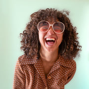 A creamy white pair of round oversized sunglasses with a light brown / pink lens.