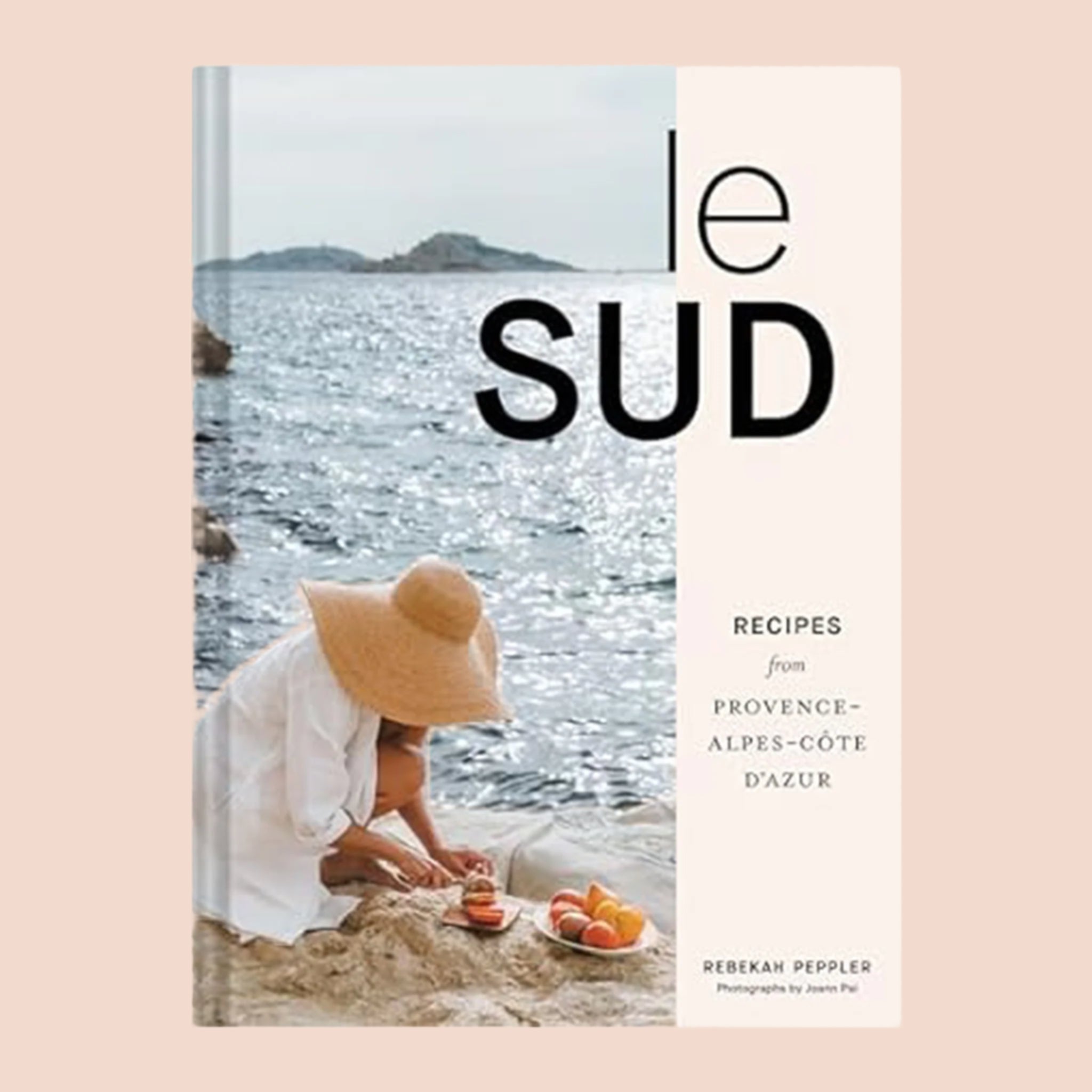 A book cover with a photo of someone cutting fruit on rocks next to the ocean and black text that reads, 'le sud Recipes from Province Alpes-Cote Dazur'. 