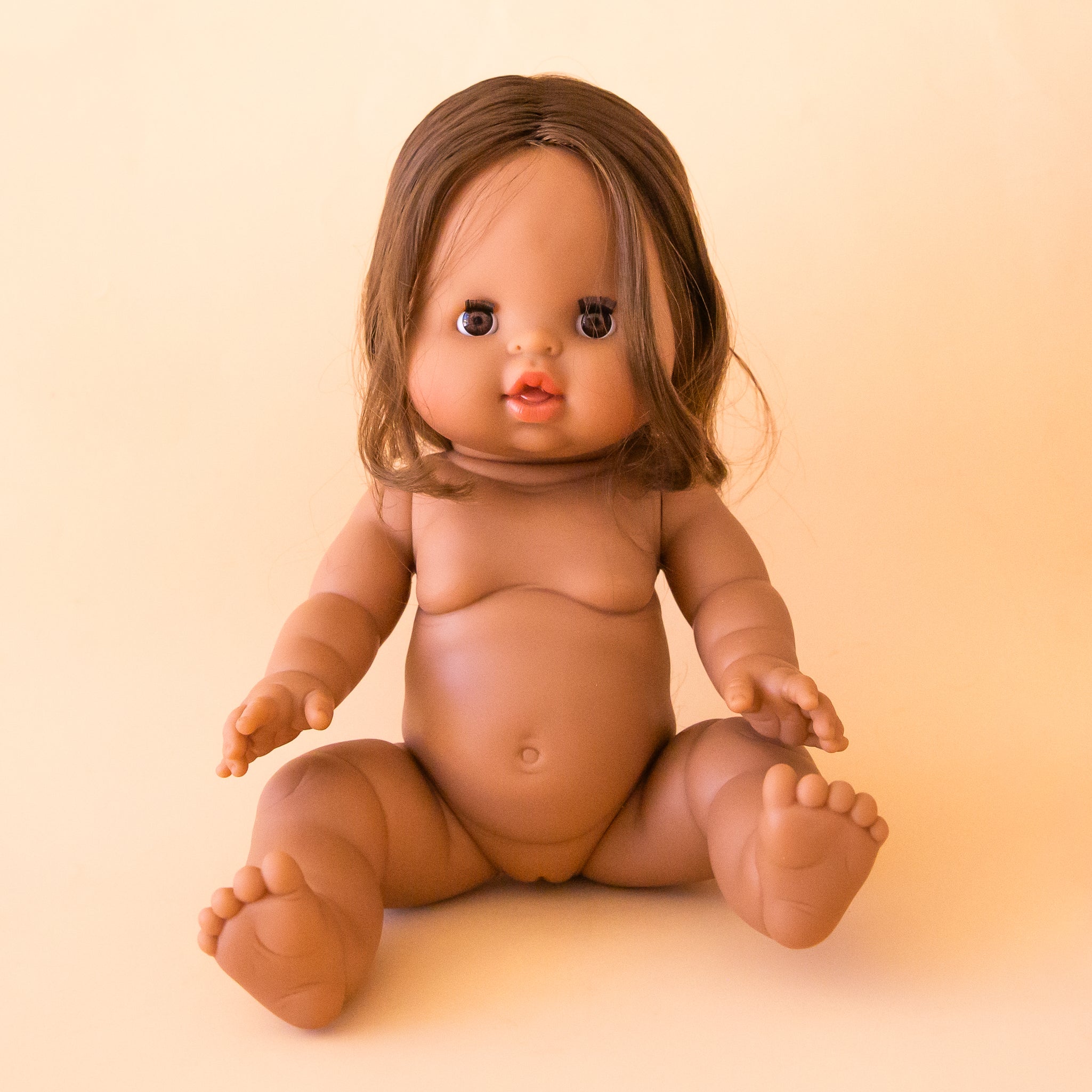 A baby girl doll with brown eyes and brown braided hair. 