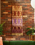 A multi colored woven wall hanging with a thin rope hanging.