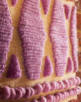 A multi colored woven wall hanging with a thin rope hanging.