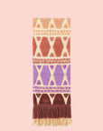 A multi colored woven wall hanging with a thin rope hanging. 
