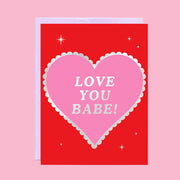 A red card with a pink heart in the center and silver foiled text that reads, 'Love You Babe!'.