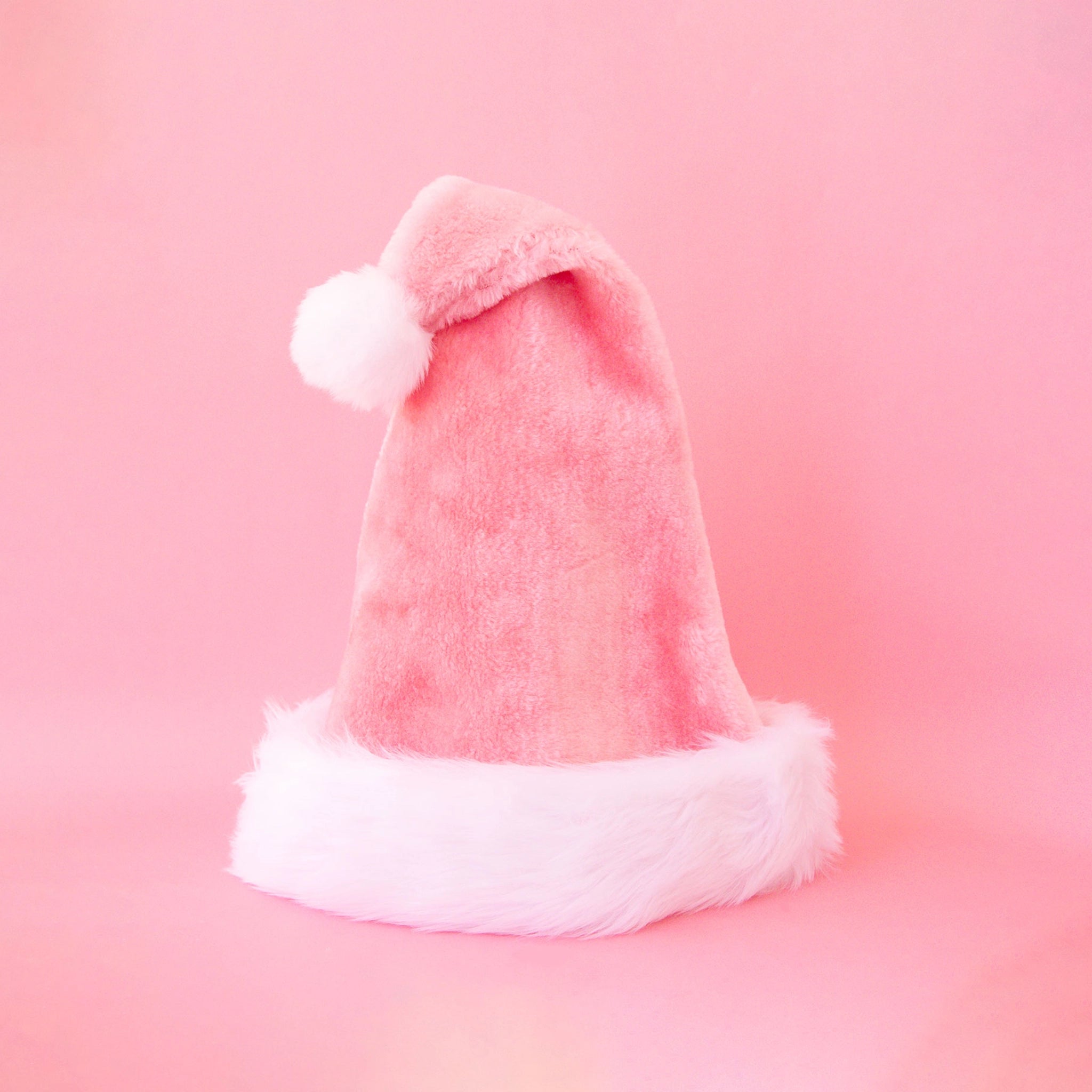 On a pink background is a pink santa hat with white faux fur detailing. 