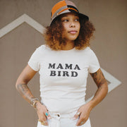 Woman wearing an off-white "MAMA BIRD" t-shirt and a hat, with tattoos on arms.