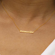 Zoomed in photo of a woman's neck. She is wearing a necklace that reads "mamacita" in lowercase script. A thin chain is connected on each side of the word.