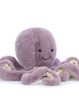 On a white background is a purple octopus stuffed animal with a smiling face. 