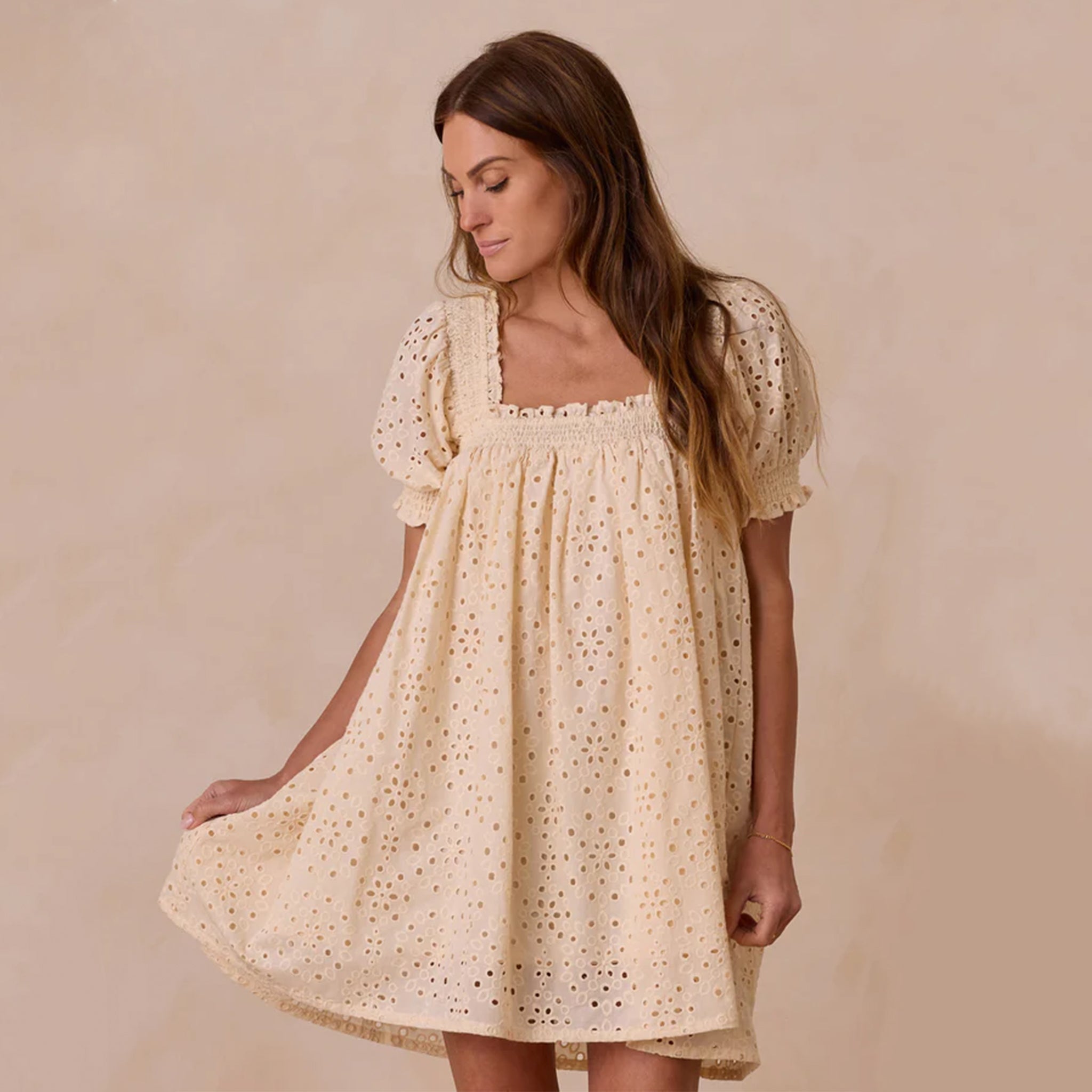 A tan mid thigh dress with an eyelet pattern and a square neckline. 