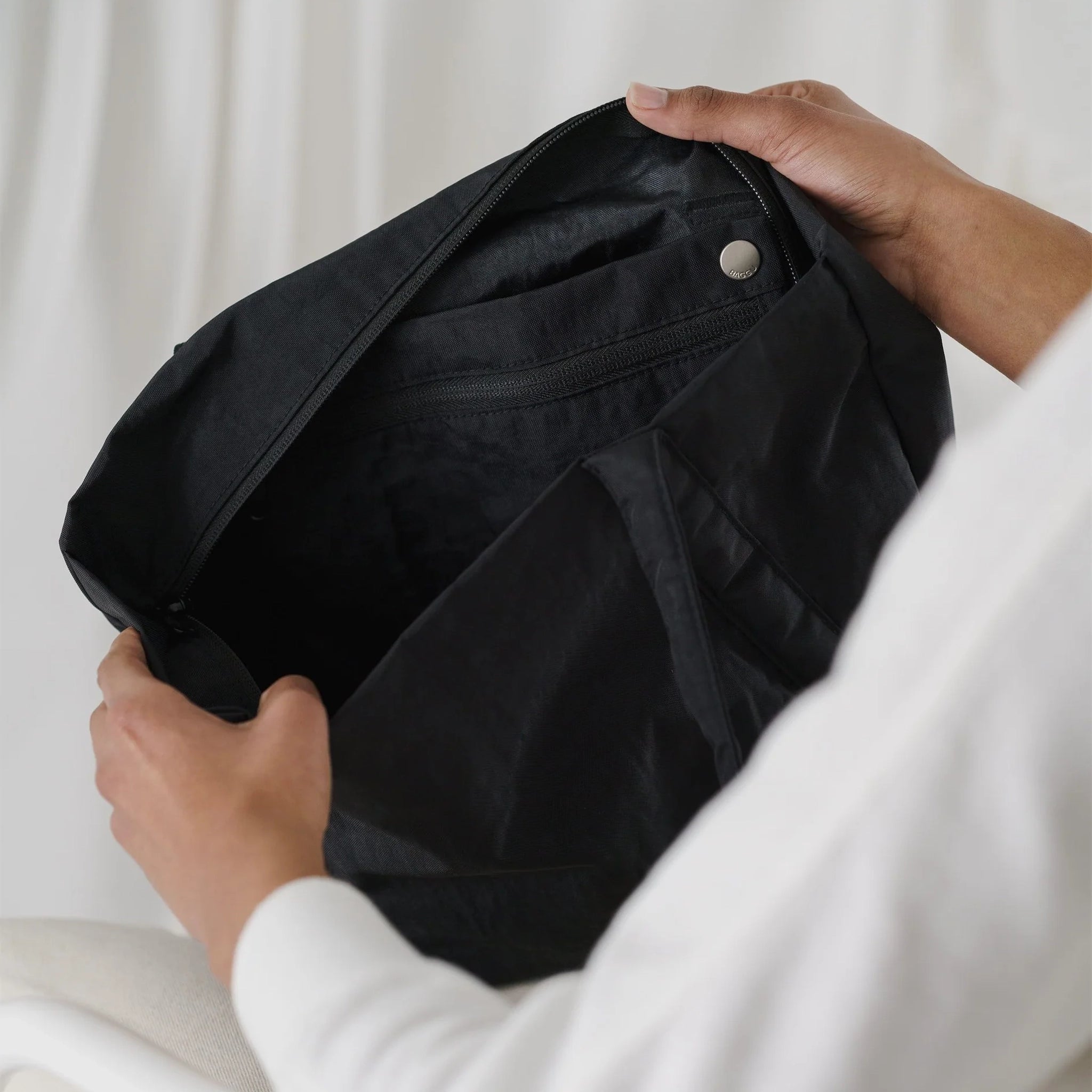 On a white background is a model opening the inside of the tote bag and showing the detachable pouch inside. 