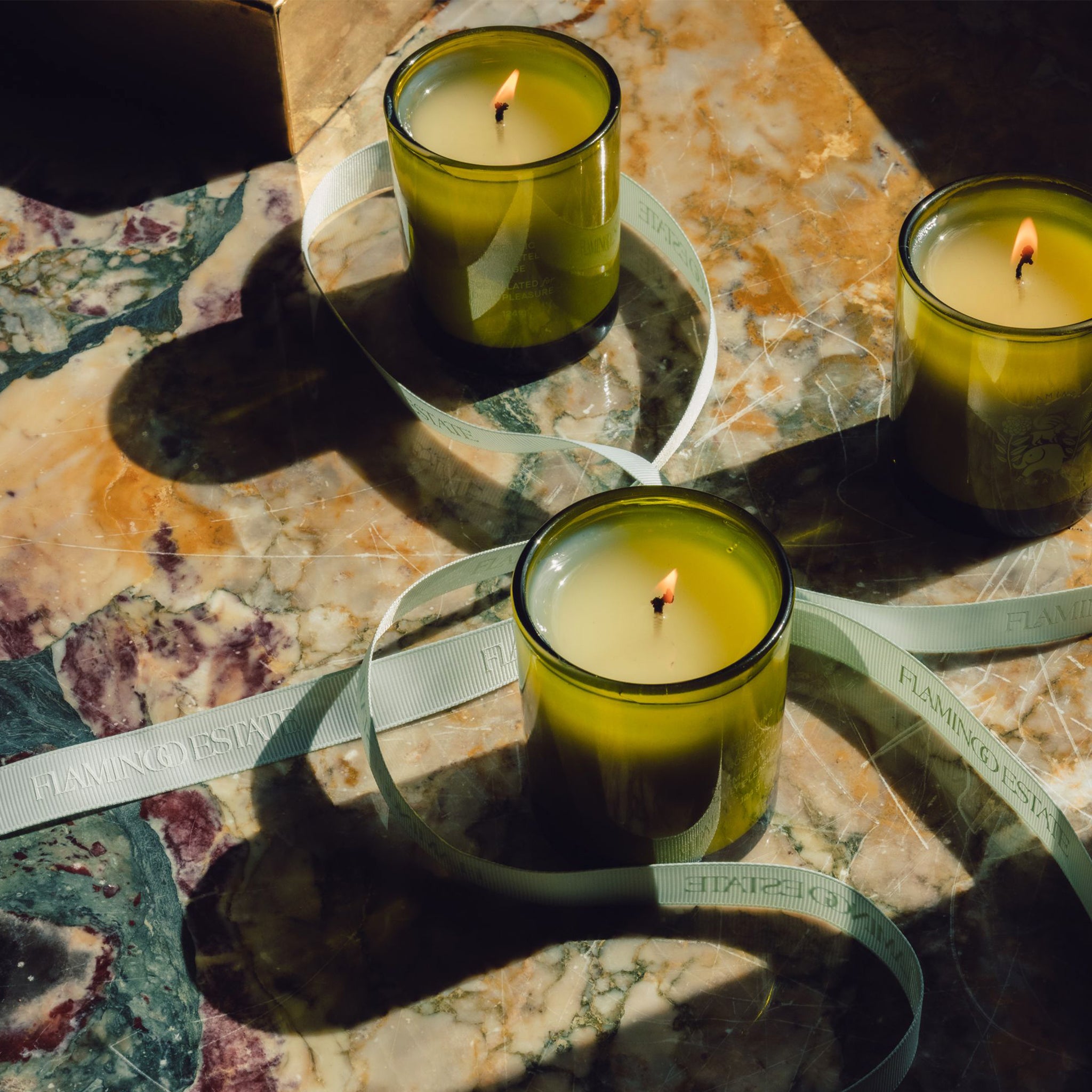 Three green glass jar candles with white labels and in a green gift box. 