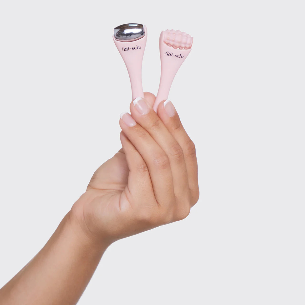 Hand holding a pink mini ice roller and a pink mini massage roller against a white background.