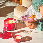 A red glass jarred candle with a matching lid. 