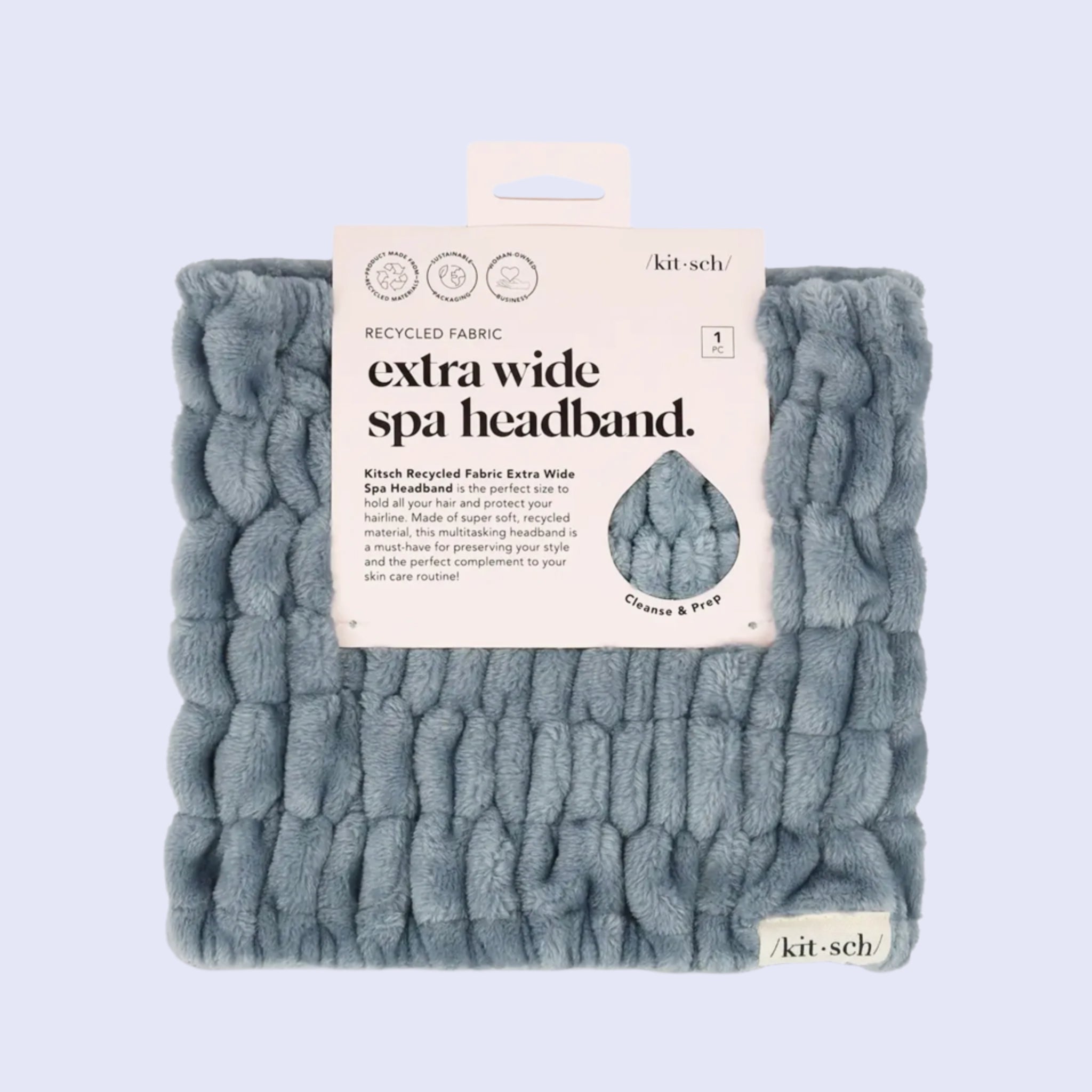 A fuzzy light blue extra wide headband folded up in its packaging that has a white label and black text that reads, "Extra Wide Spa Headband".