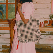 A black and white gingham print tote bag with ruffle details and shoulder straps. 