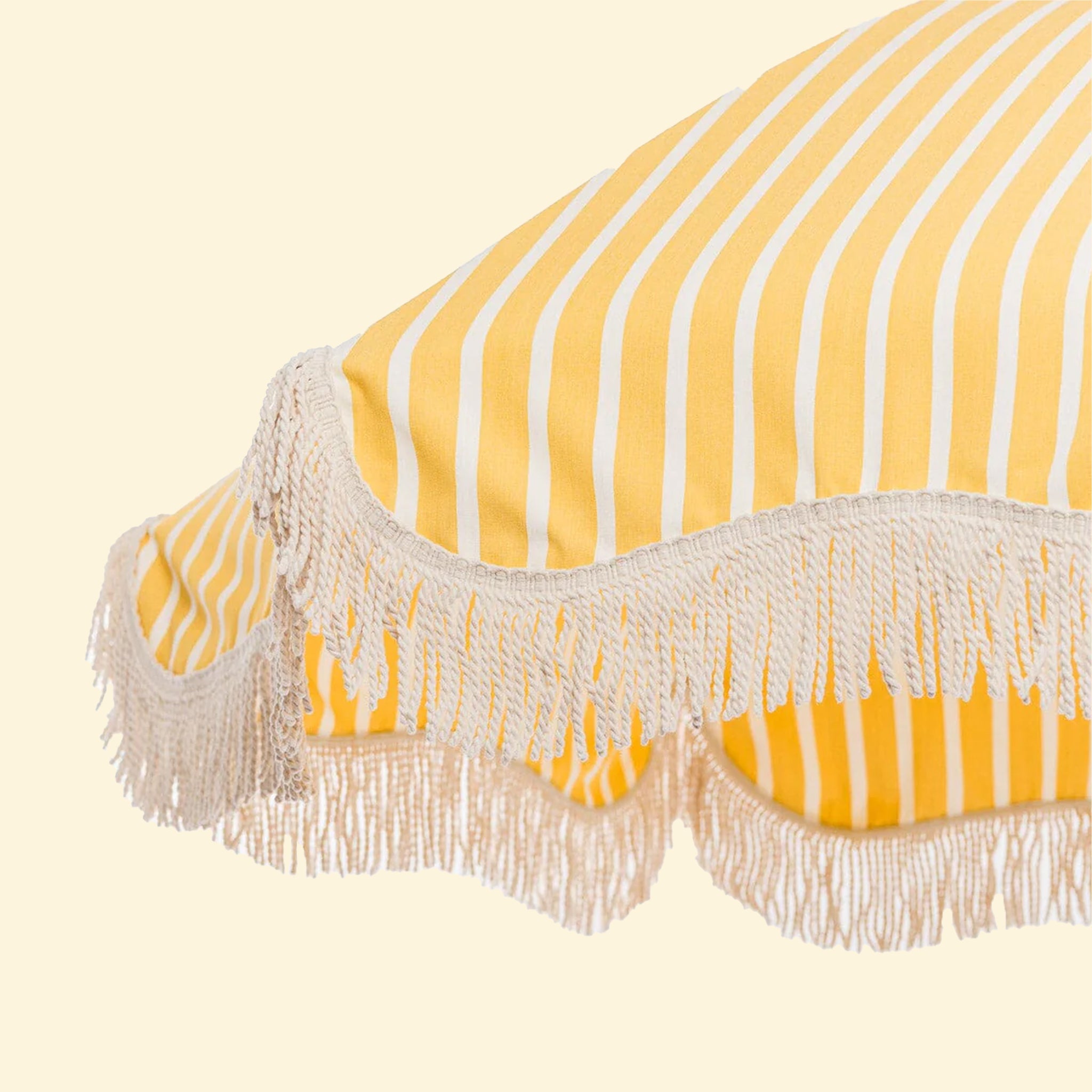 A white and yellow striped outdoor umbrella with a rope fringe detail around the edge. 