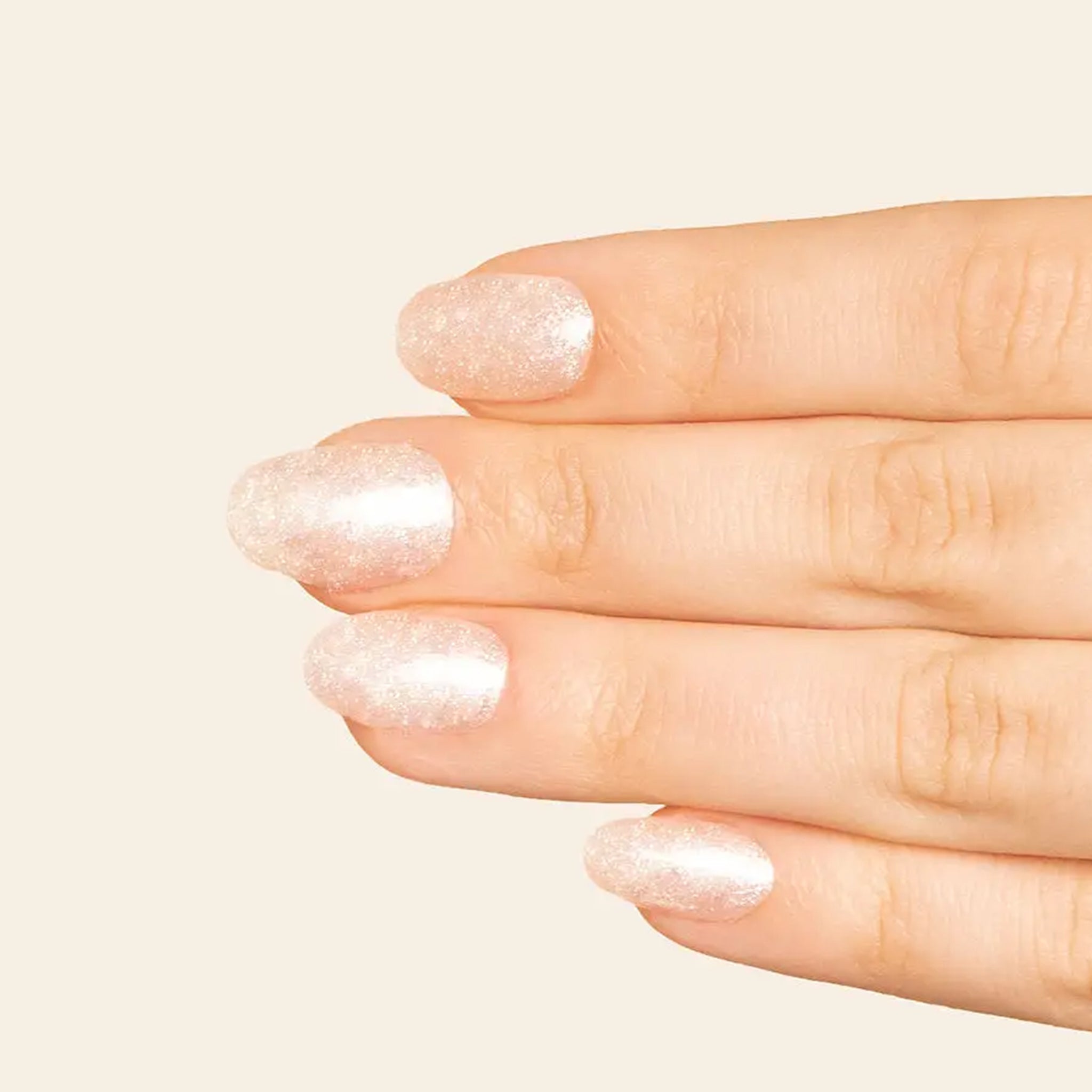 A clear, glittery nail polish with a light pink tint in a rectangle glass bottle. 