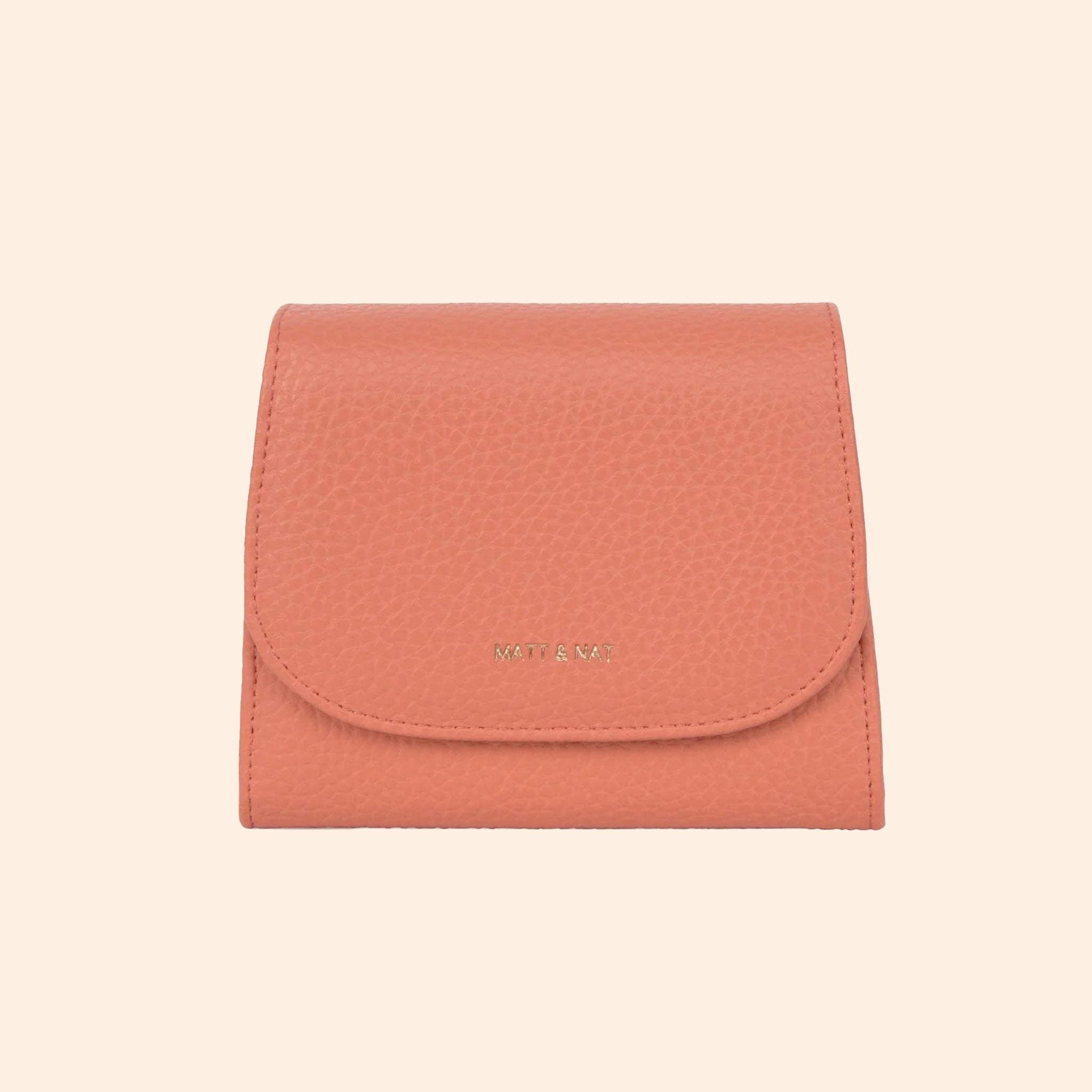 A light pinkish orange vegan leather wallet with a thin removable crossbody strap. 