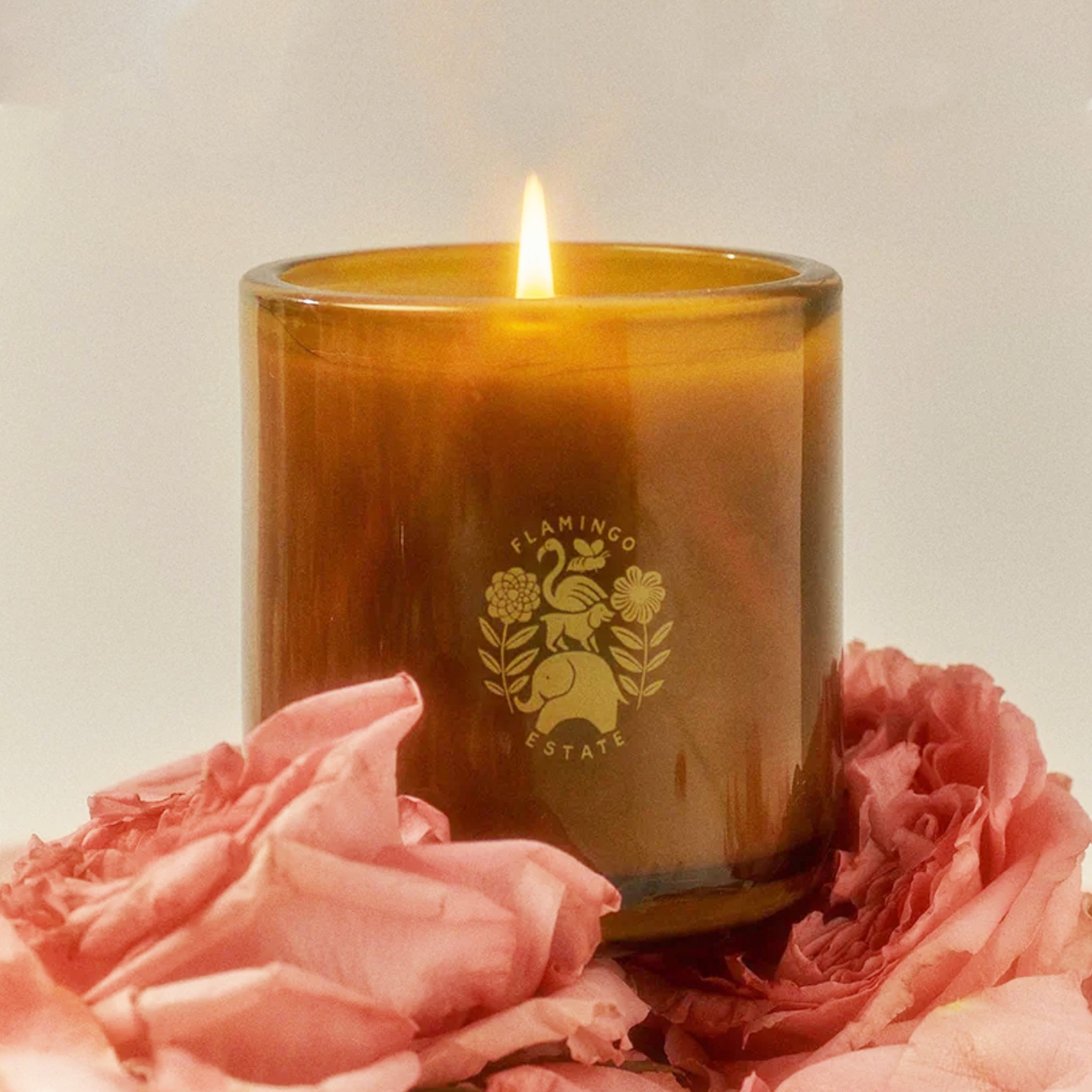 The back of the green glass jar candle with a Flamingo Estate logo on the front that features a flamingo, dog and elephant graphic in the center. 