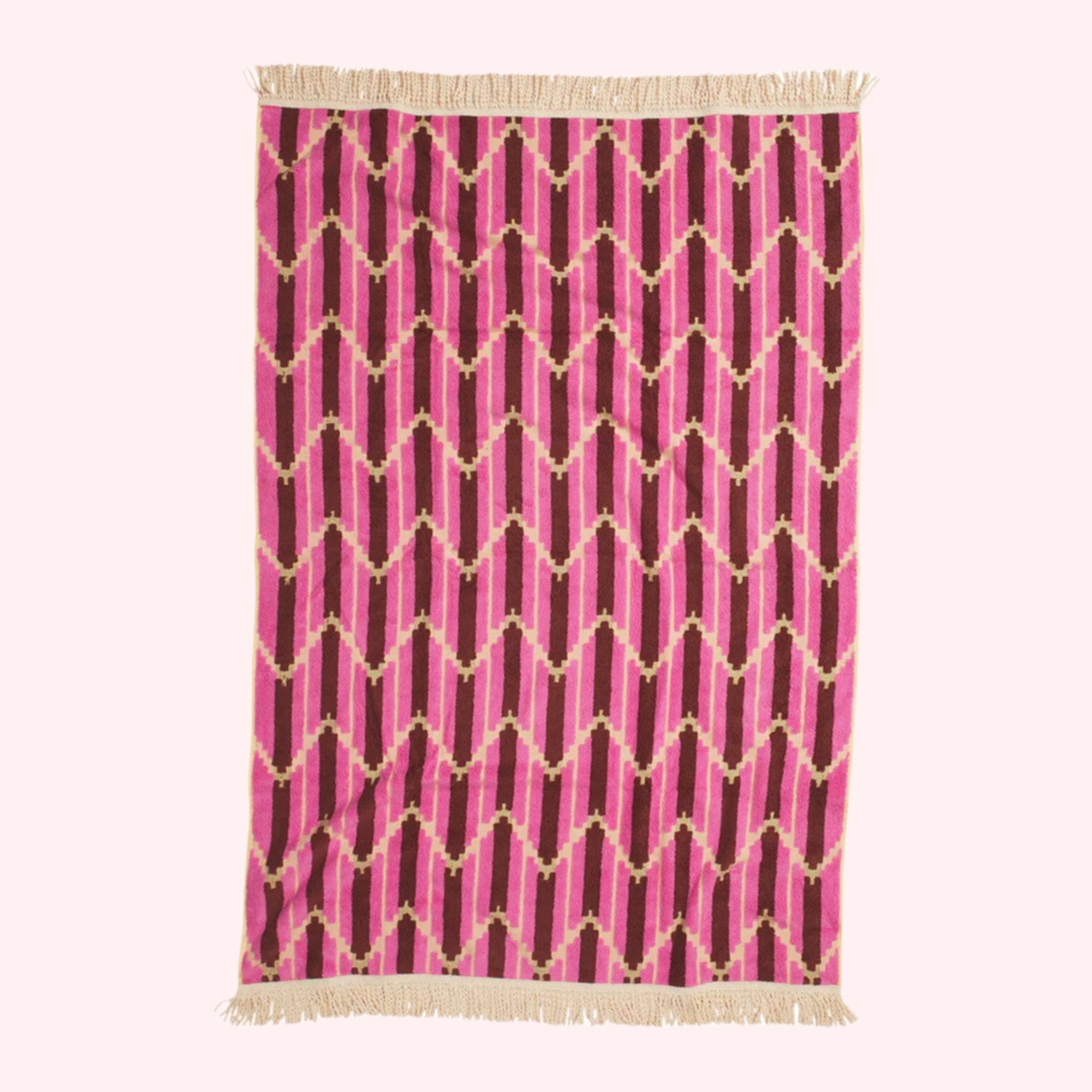 A pink chevron print towel with an ivory tassel edge on two sides. 