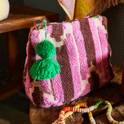 A pink terry cloth pouch with a green tassel on the zipper closure. 