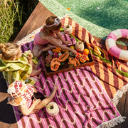 A pink chevron and striped print towel with an ivory tassel edge on two sides. 