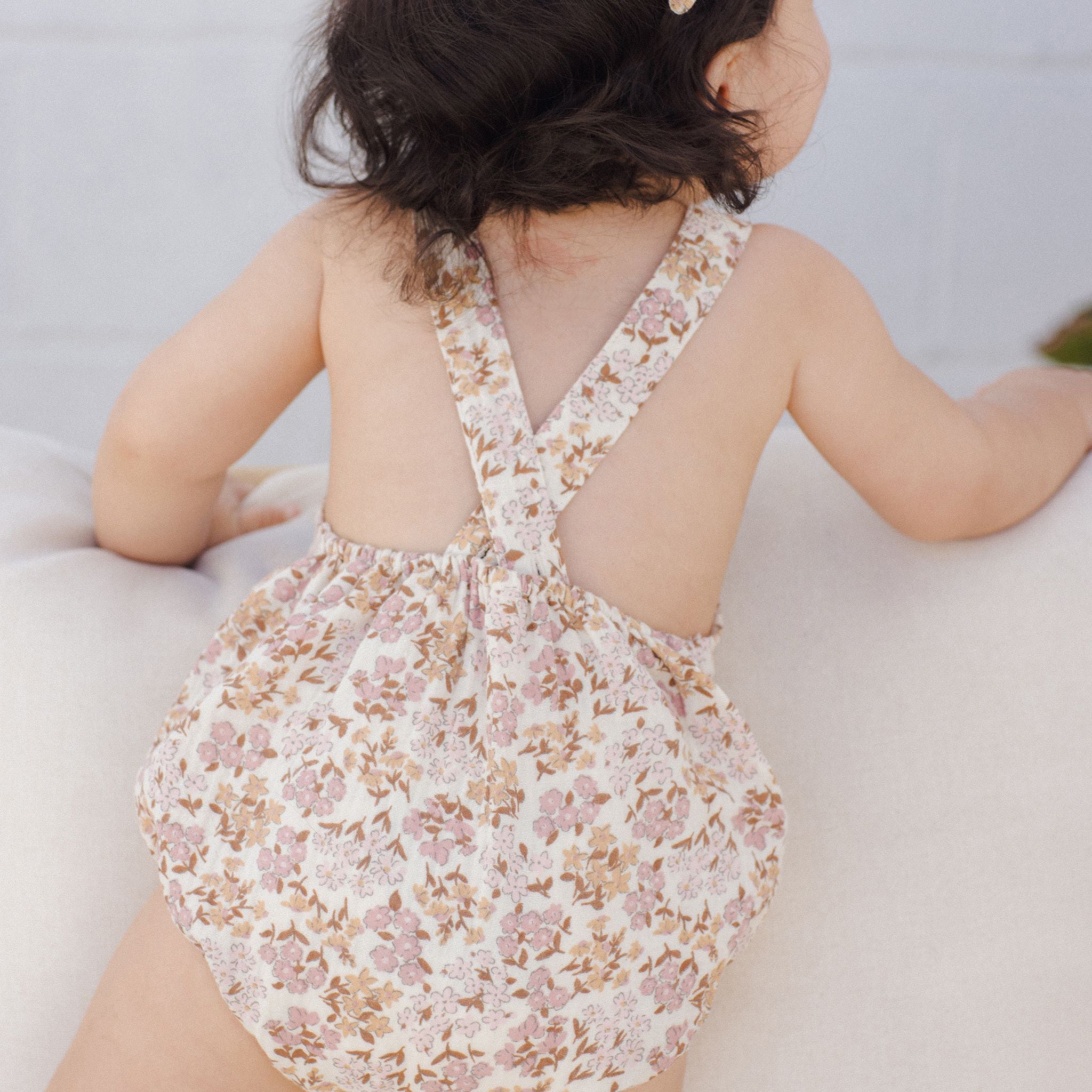 A children&#39;s romper with a light pink and yellow floral pattern. 