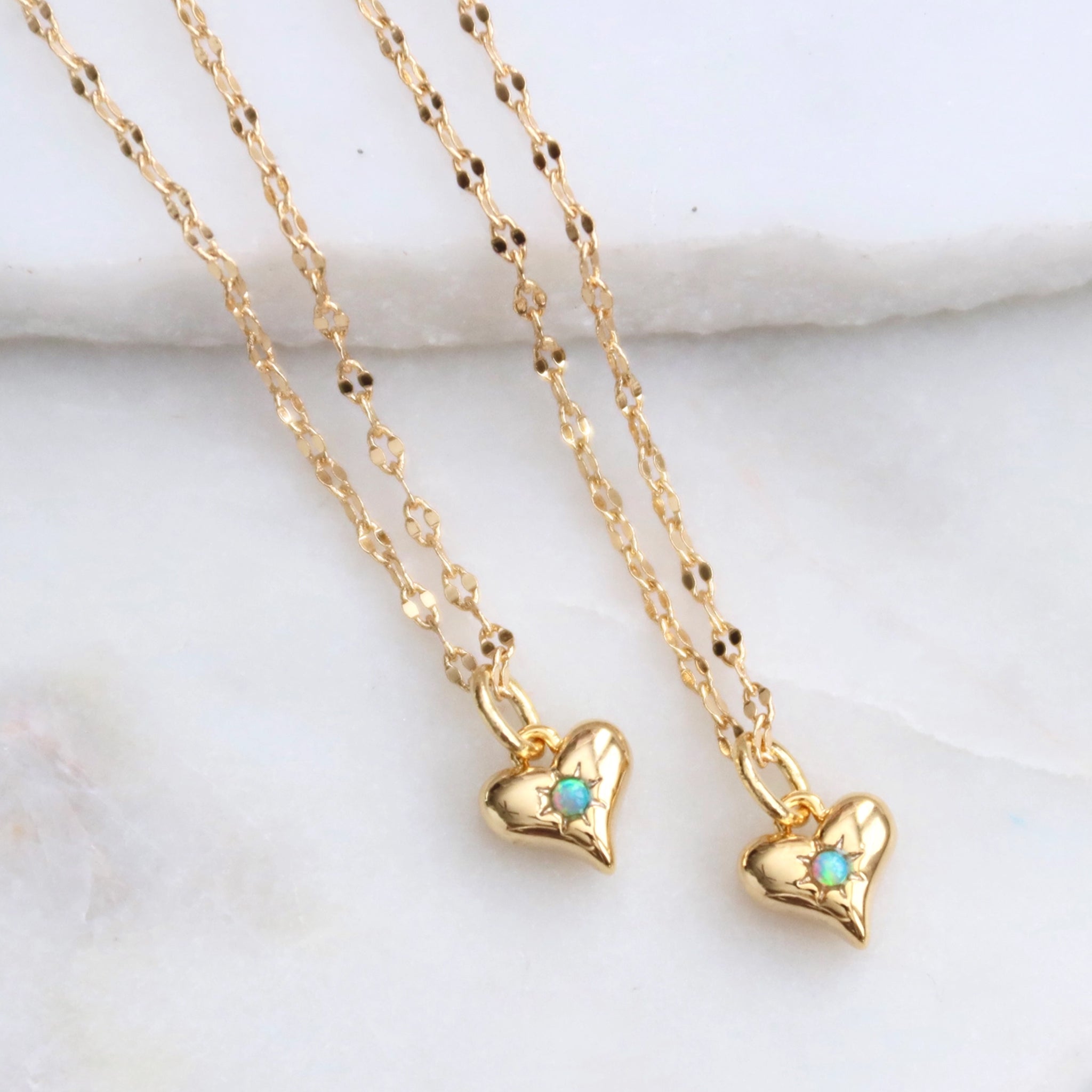 A gold chain necklace with a small gold heart shaped pendant with a blue opal in the center. 