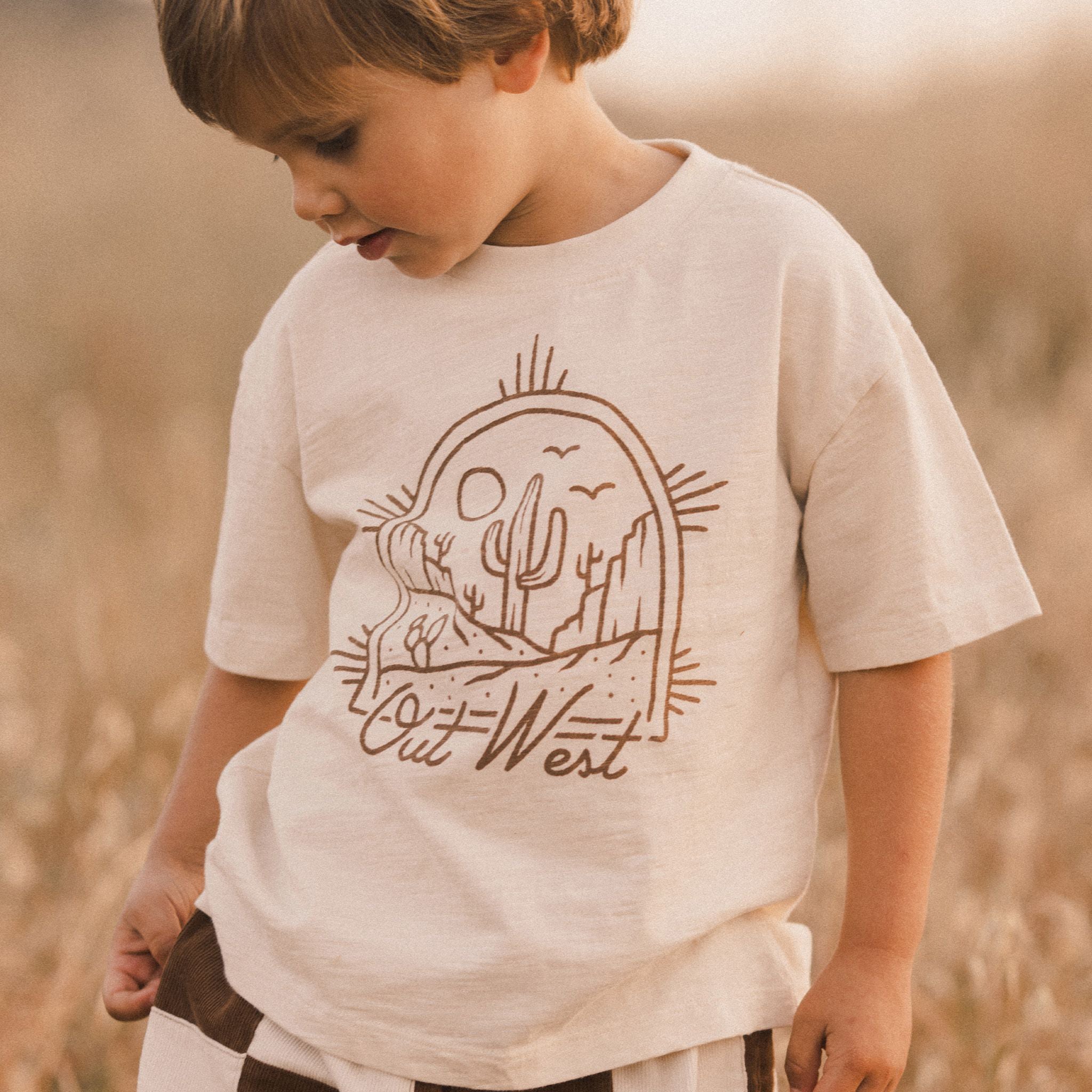 An ivory t-shirt for children with a brown western graphic on the front that reads, "Out West".