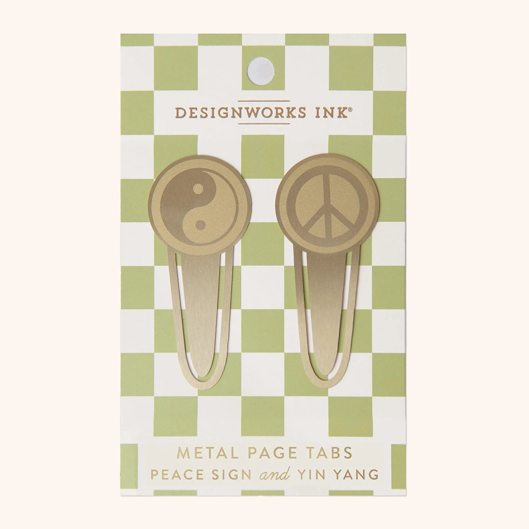 On a white background is a green and white cardboard packaging that is holding two gold book tabs in the shape of a yin and yang symbol and the other a peace sign. 