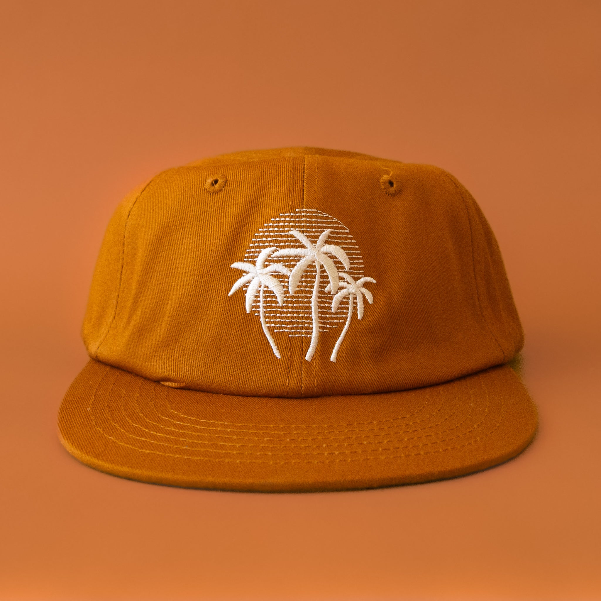 A burnt orange flat brim hat with a white embroidered palm logo. 