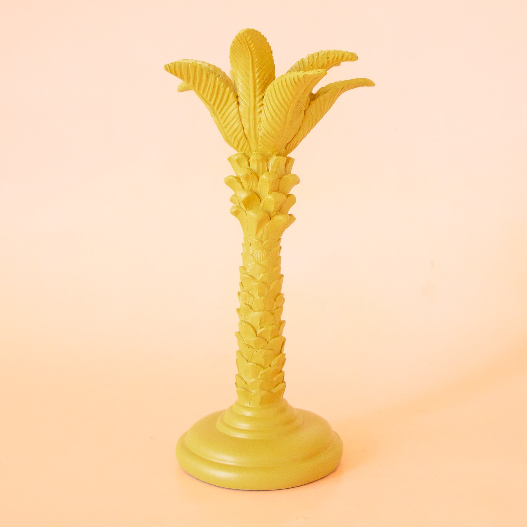 A yellow colored palm tree shaped taper candle holder. 