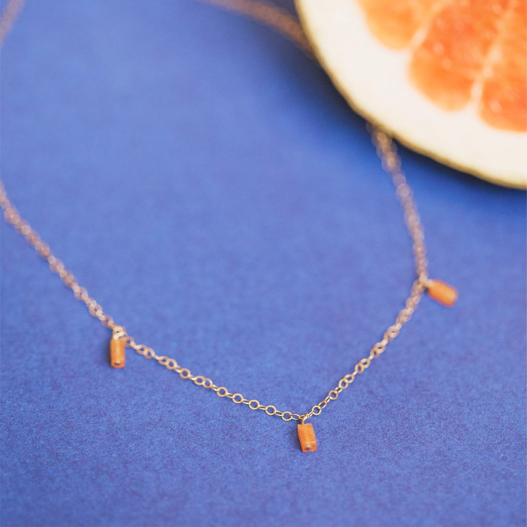 A gold necklace with three burnt orange stones hanging from different points on the chain. 