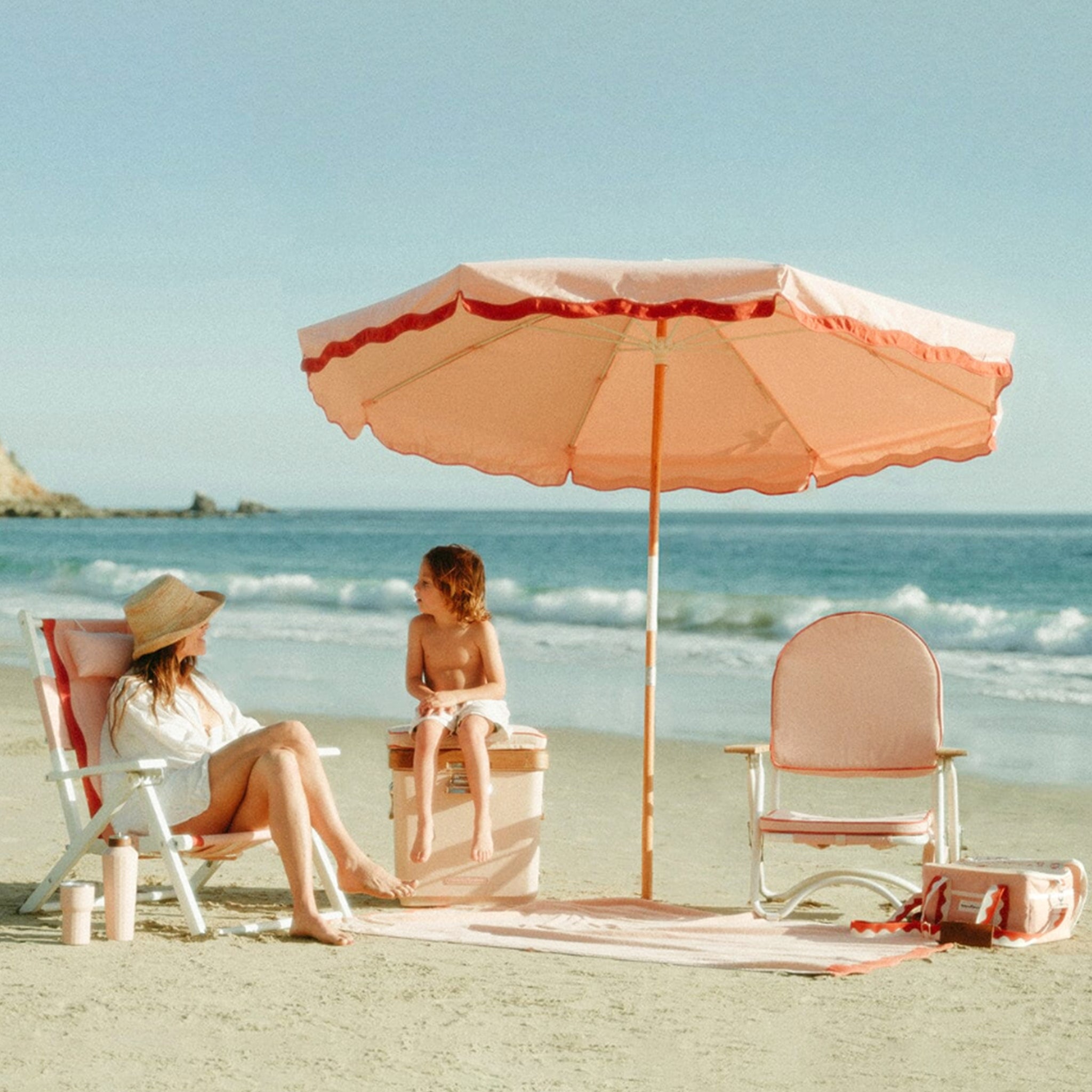 A pink arched folding beach chair with a reddish/dark pink lining around the edge and wood arm rests. 