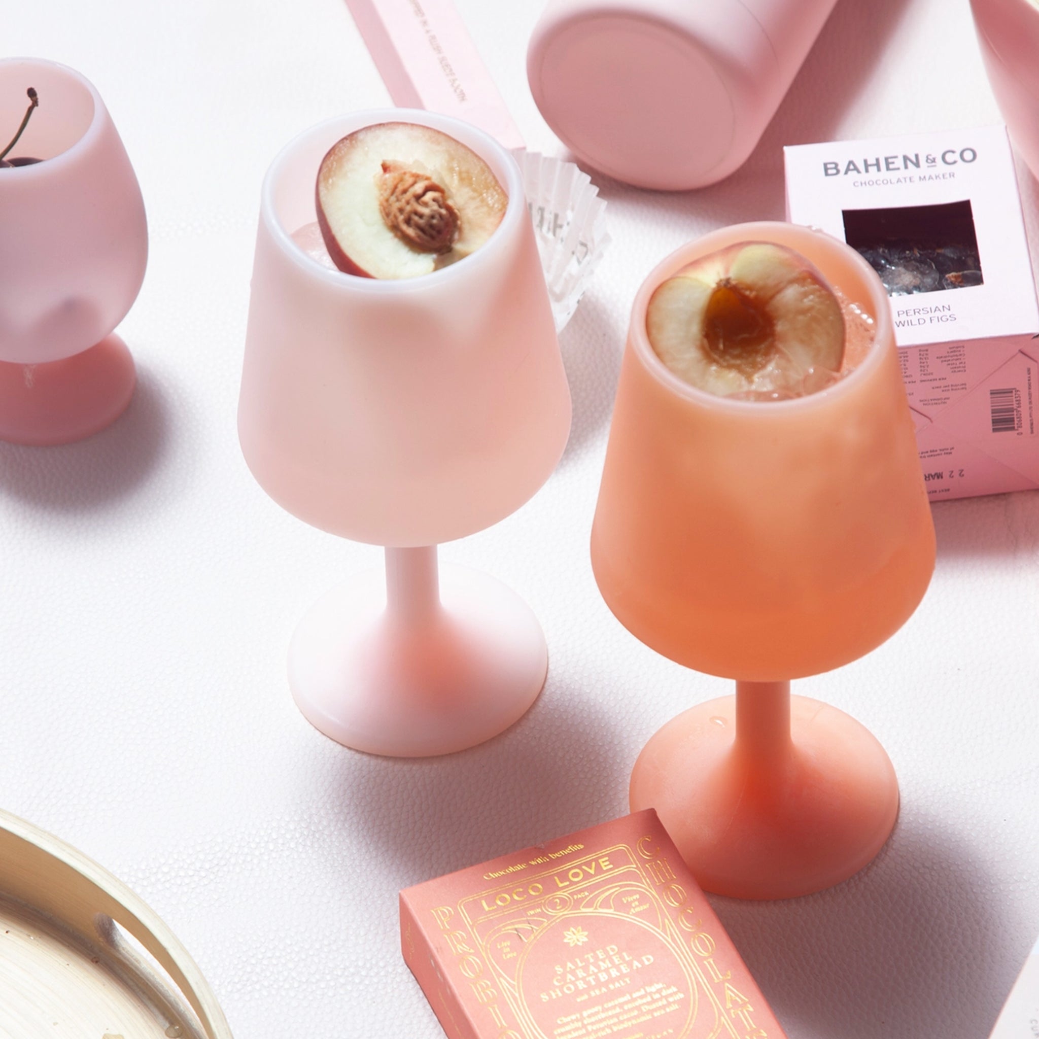 A pair of silicone wine glass shaped cups in a peach shade and a light pink shade. Photography props not included with purchase. 