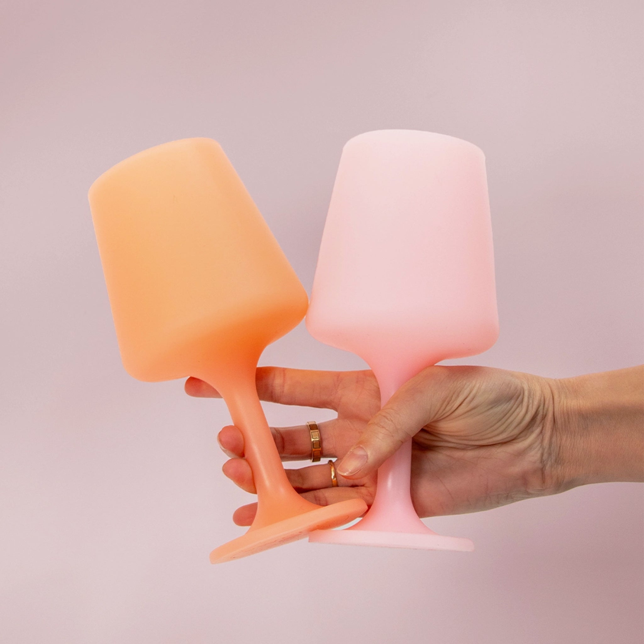 A pair of silicone wine glass shaped cups in a peach shade and a light pink shade. Photography props not included with purchase. 