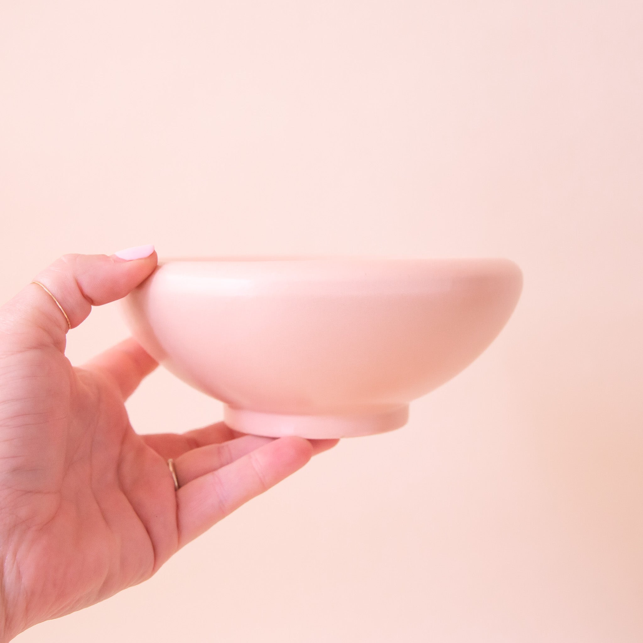 A light pink ceramic low bowl planter with a rounded edge. 