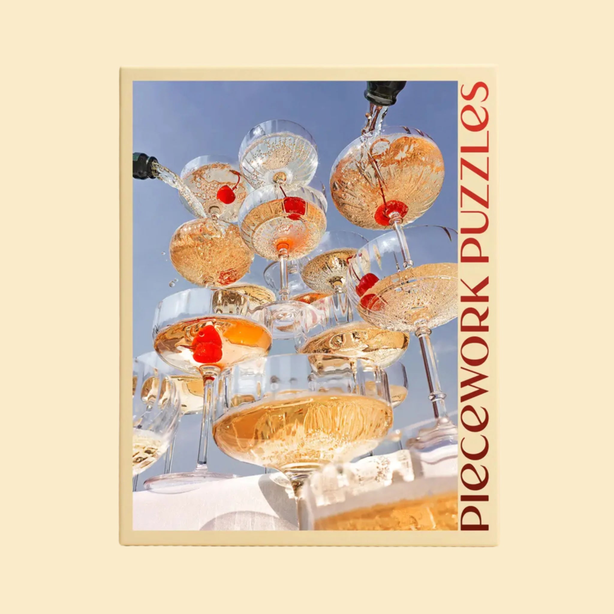 A yellow puzzle box with a photograph of a champagne tower with cherries at the bottom and text that reads, 'Piecework Puzzles'. 