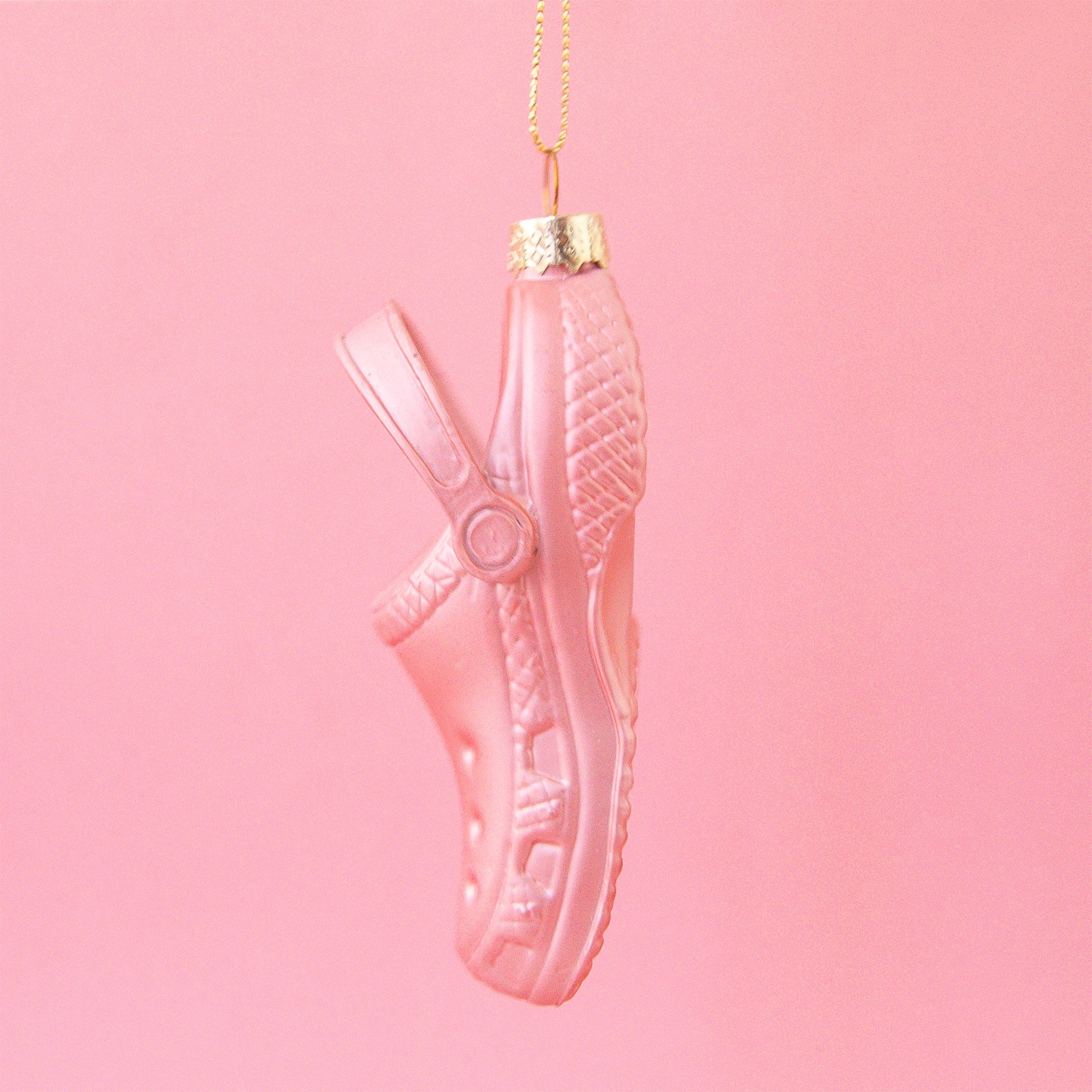 On a pink snowy background is a pink glass ornament in the shape of a clog shoe.