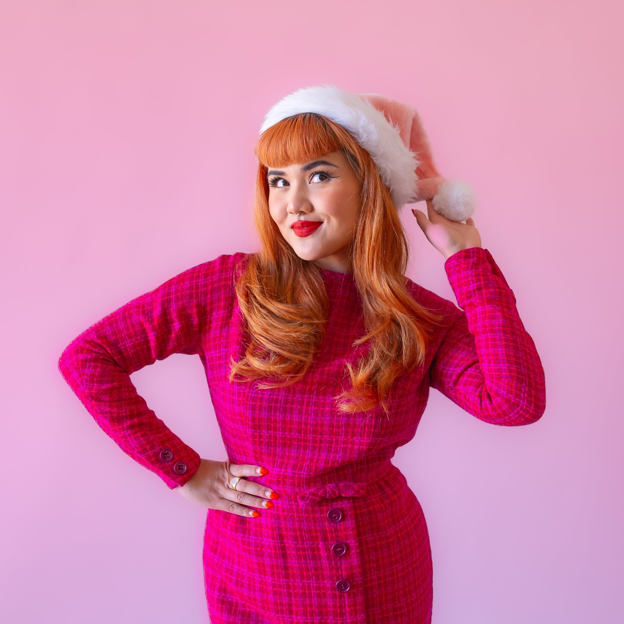 On a pink background is a model wearing pink santa hat with white faux fur detailing.