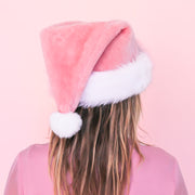 On a pink background is a pink santa hat with white faux fur detailing.