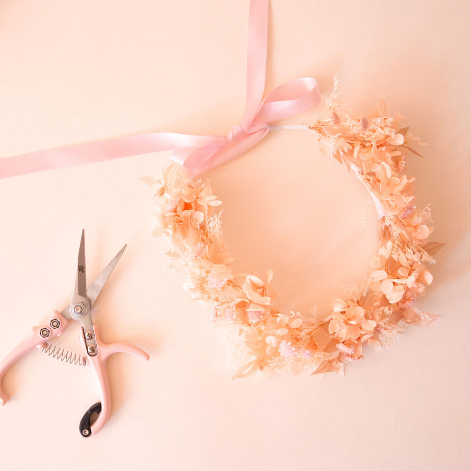 A neutral dried floral flower crown next to pruning shears. 
