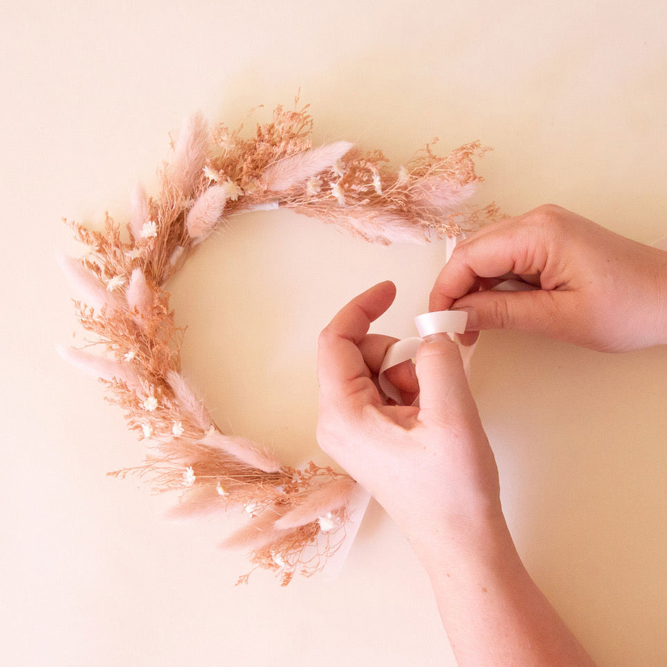 A neutral dried floral flower crown being crafted by someone&#39;s hands. 