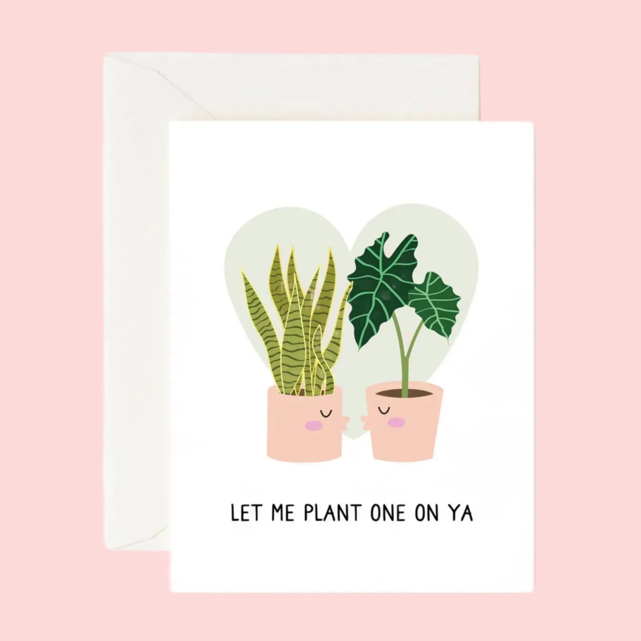 A white card with a light grey heart in the background behind a snake plant and an Alocasia Polly that are planted in two separate pink pots that have kissing faces and are going in for a kiss. There are black words underneath that read, &quot;Let Me Plant One On Ya&quot;