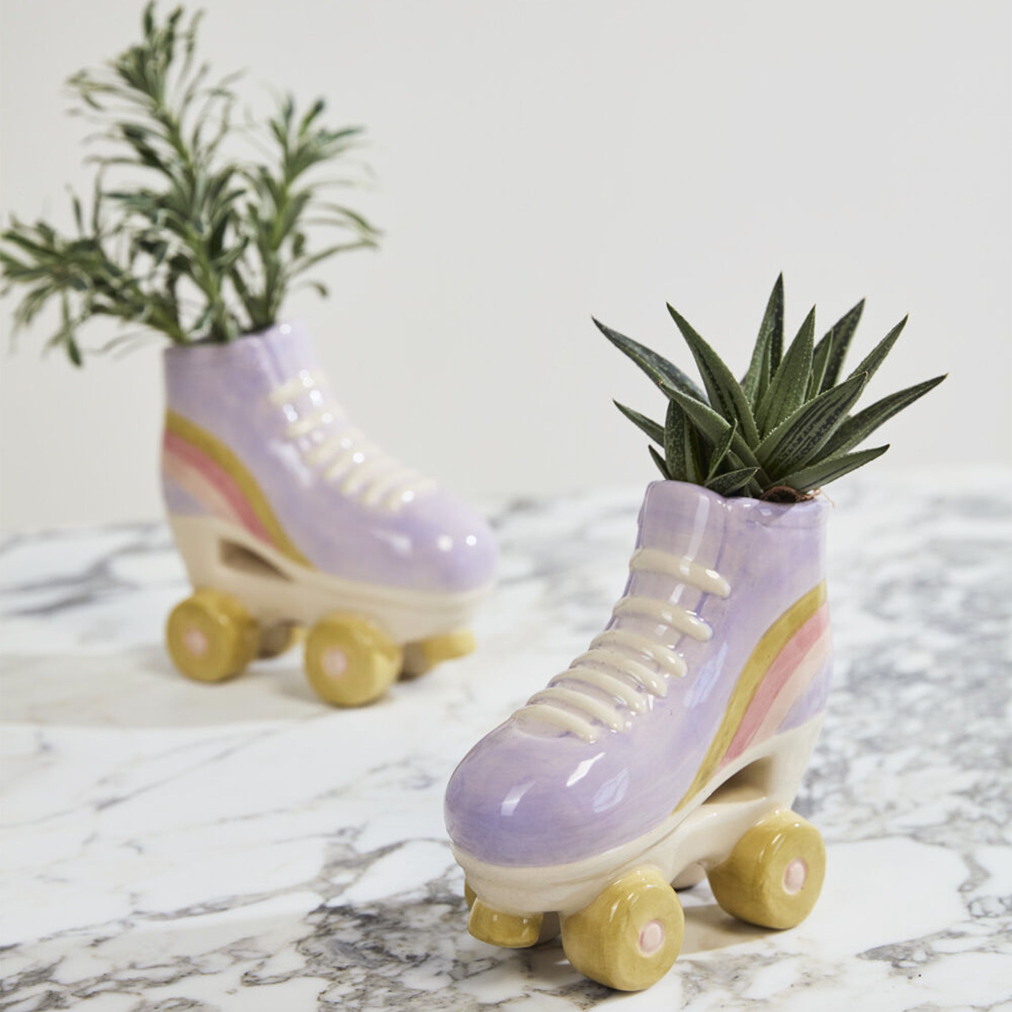 A purple ceramic roller skate shaped planter with yellow and pink details. Plants photographed not included with purchase. 