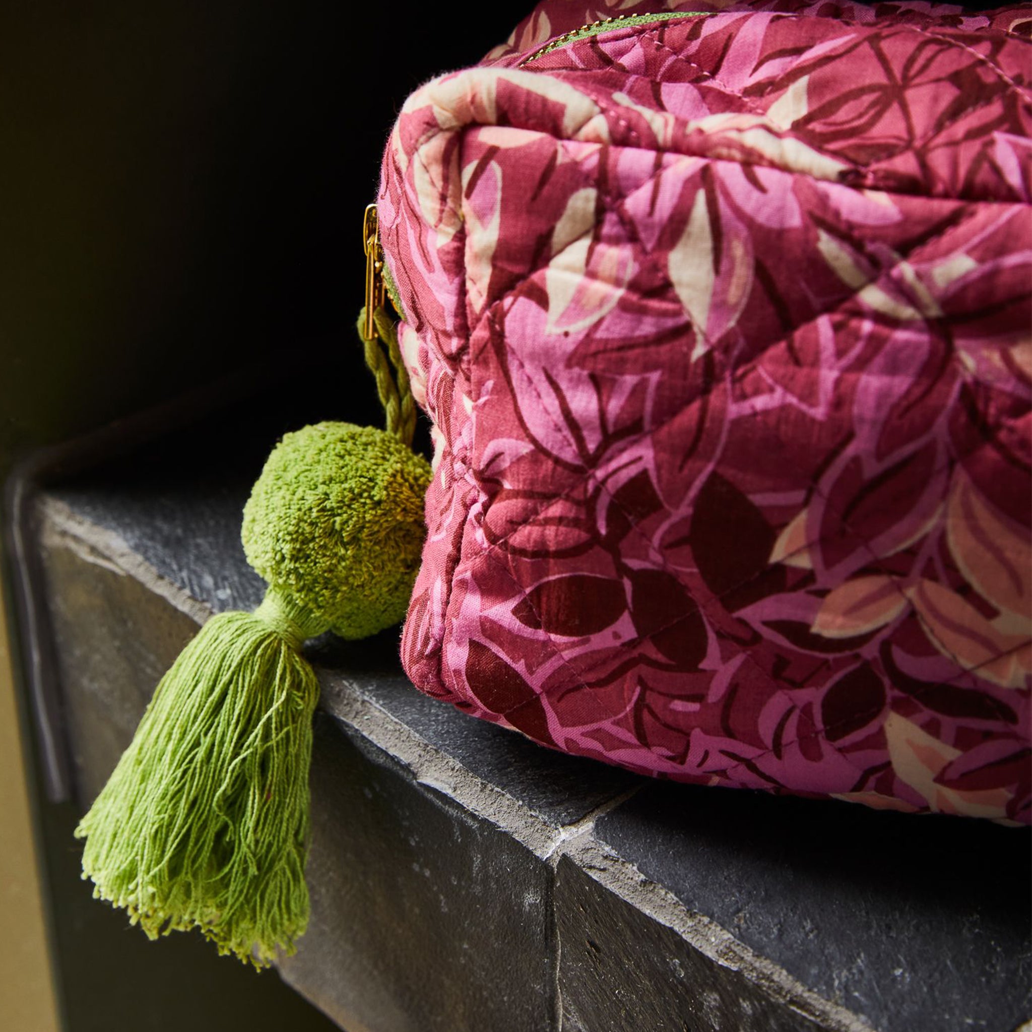 A pink floral patterned cosmetic bag with a green tassel zipper. 