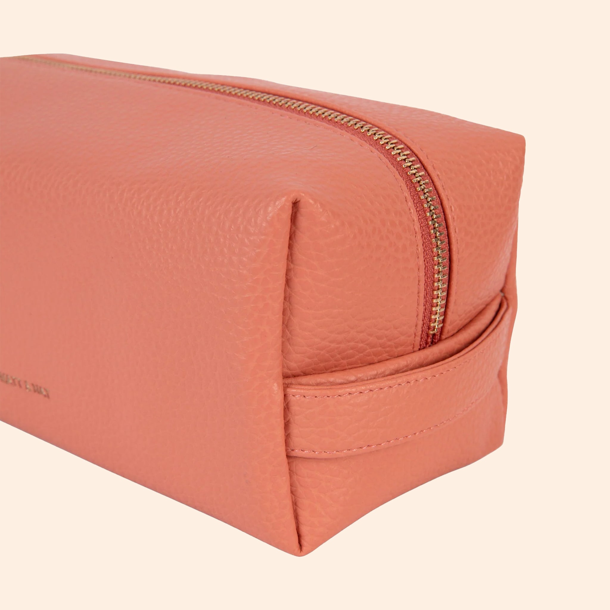 A peachy pink vegan leather cosmetic case with a zipper closure. 