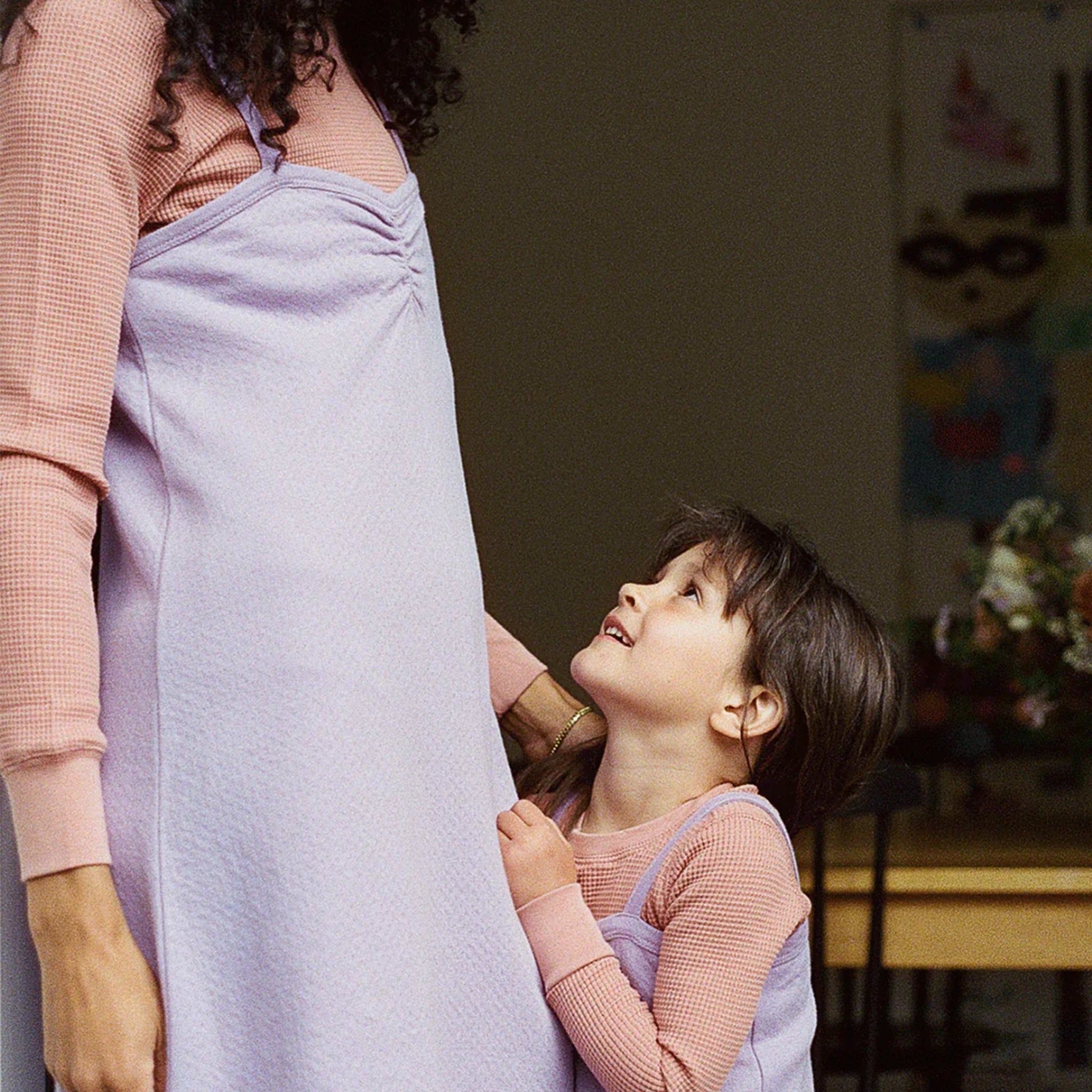 On a white background is a model wearing a lavender pointelle dress standing next to a children's model wearing a matching lavender dress. 