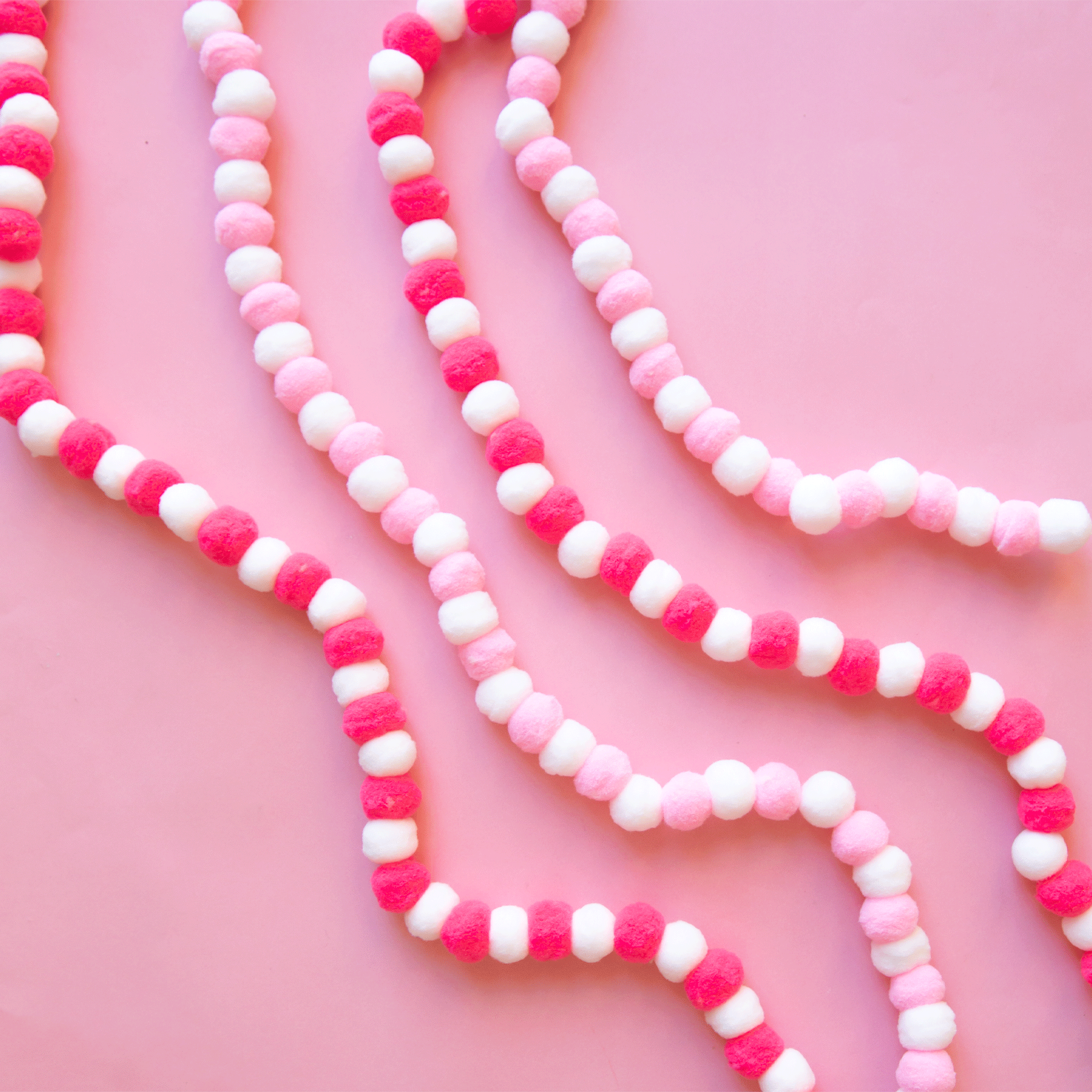 On a light pink background is both color ways of the pom pom garland. One is hot pink and white and the other is baby pink and white. 