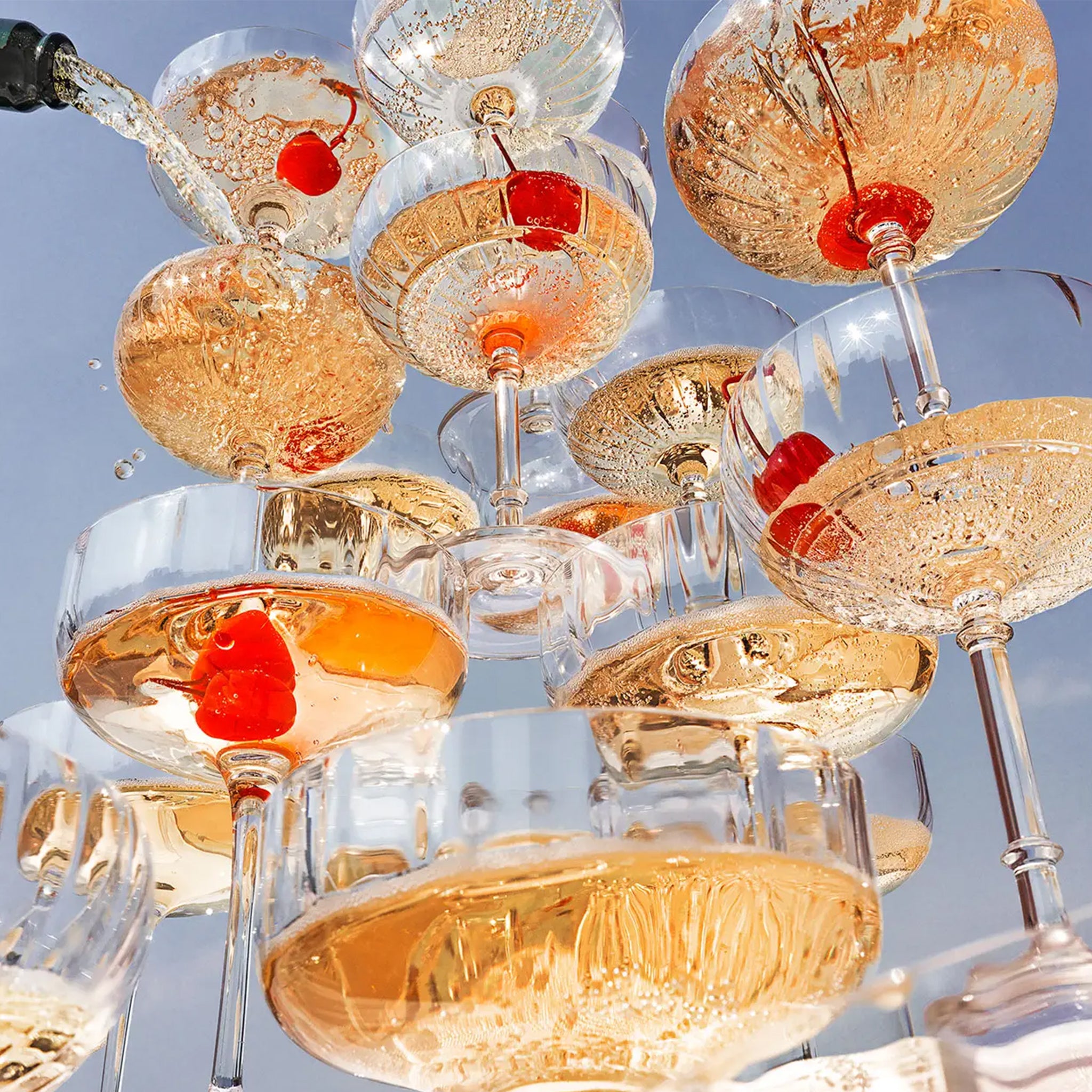 A photograph of a champagne tower with cherries at the bottom of the coupe glasses. 