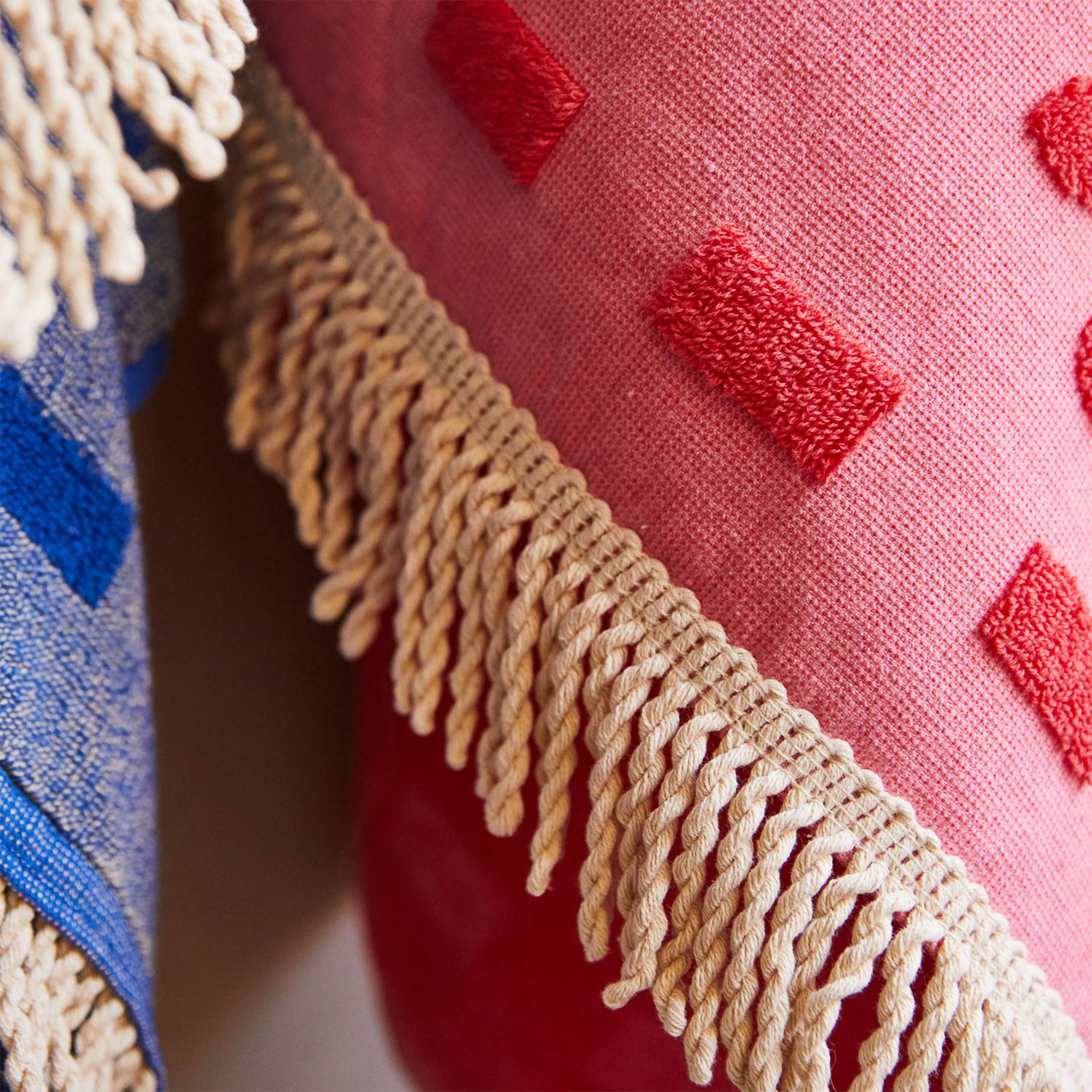 A pink bath towel with a floral print and fringe details on two edges. 